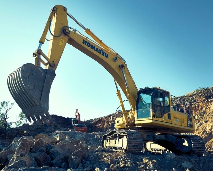 Komatsu excavator with grapple bucket on quarry edge under blue skies